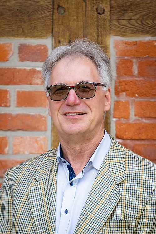 Älterer Mann mit Brille vor Backsteinwand
